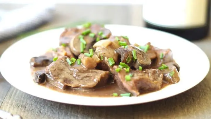 a close up of beef tips and sliced mushrooms in a sauce on a white plate