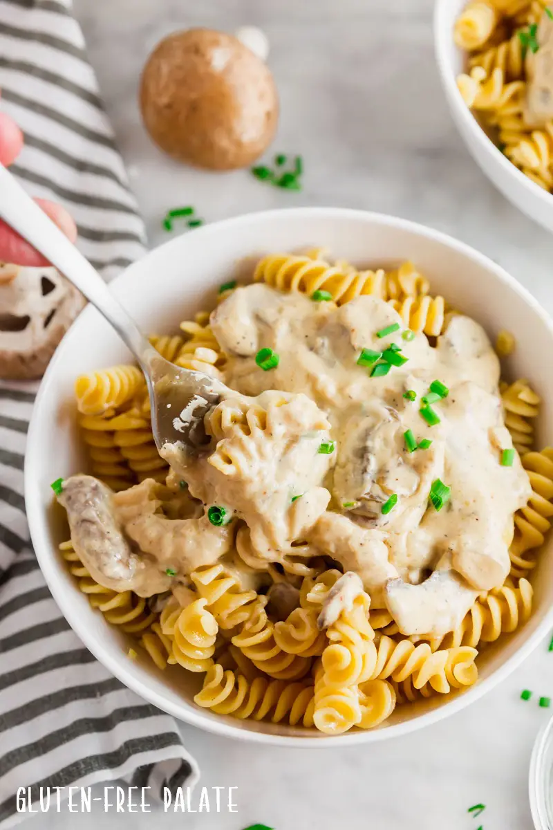 gluten free stroganoff sauce over noodles in a white bowl with a fork taking a bite out