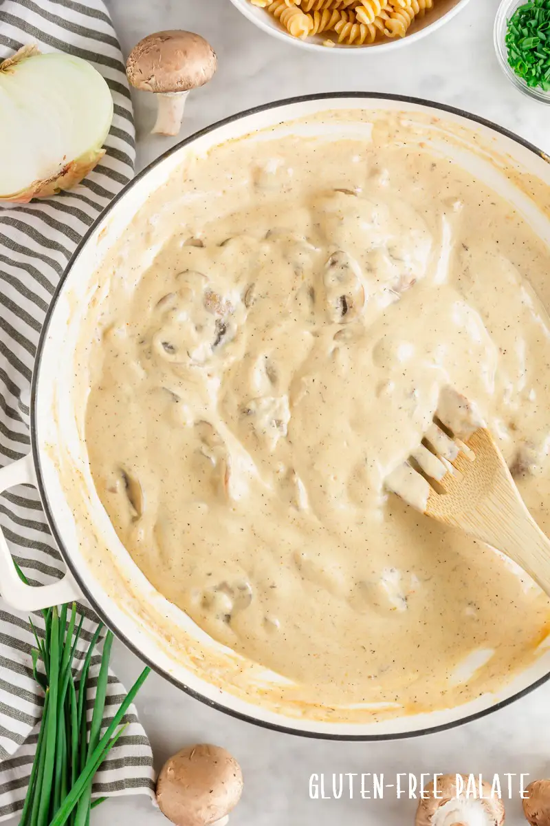 a pan of mushroom stroganoff sauce with a wooden spoon stirring