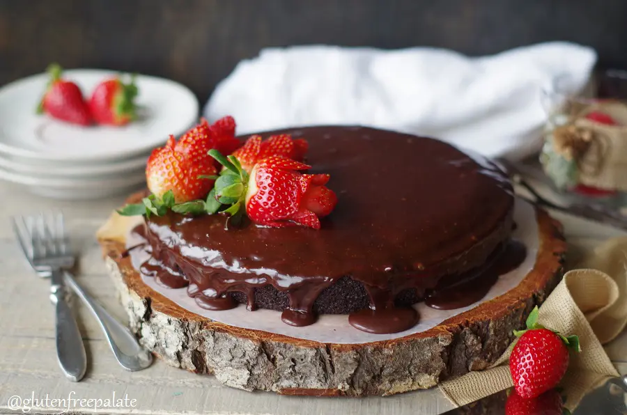 a Gluten-Free Vegan Chocolate Ganache Cake topped with strawberry roses, served on a wood cake platter