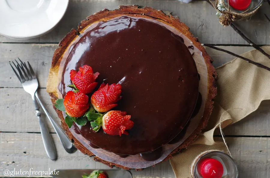 a top down view of a Gluten-Free Vegan Chocolate Ganache Cake topped with strawberry roses, served on a wood cake platter
