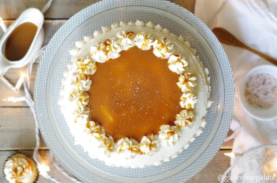 a top down view of a caramel cake topped with white frosting and caramel on a silver cake plate