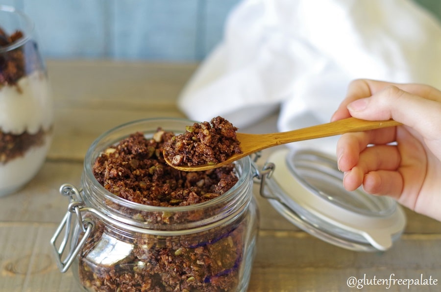 Paleo Granola in a glass jar with a hand holding a wooden spoon with granola