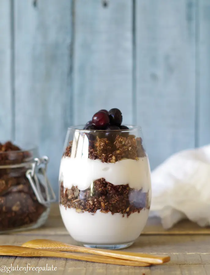 a close up of Paleo Granola layered with yogurt in a glass jar with a wooden spoon