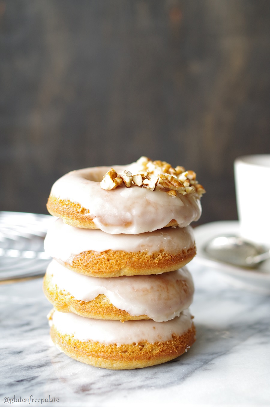 four Gluten-Free Dairy-Free Maple Donuts stacked and topped with pecans on a marble counter