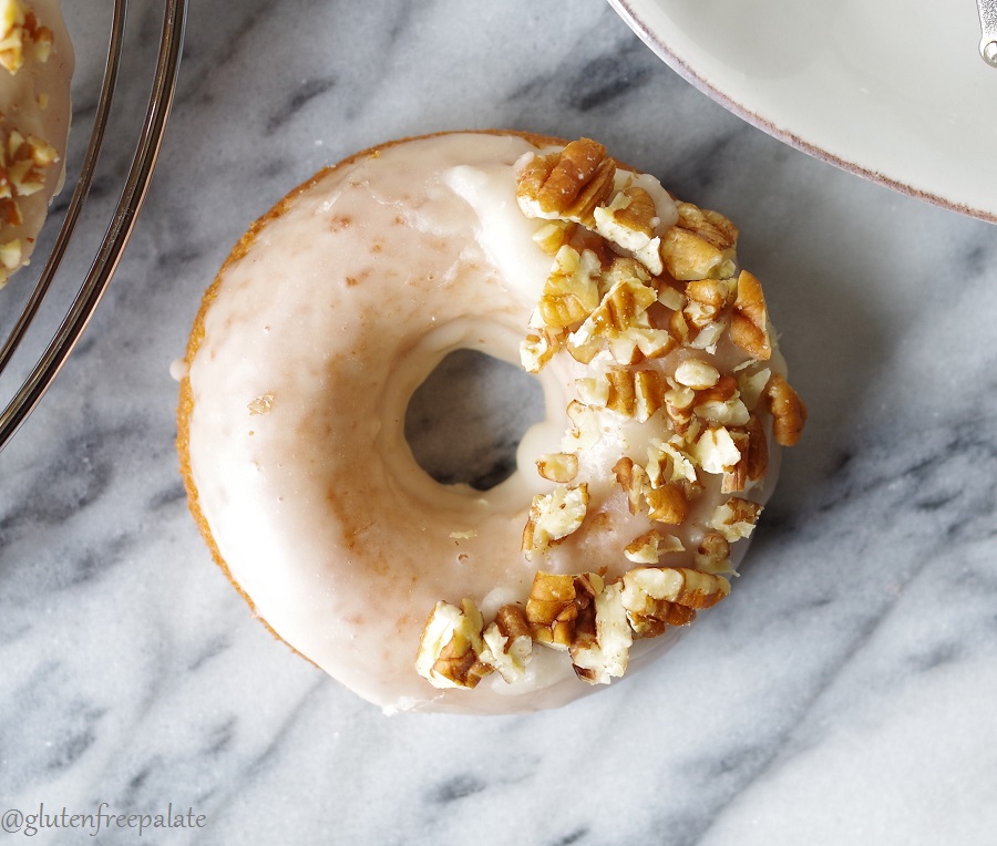 a close up of a maple donut topped with icing and chopped pecans