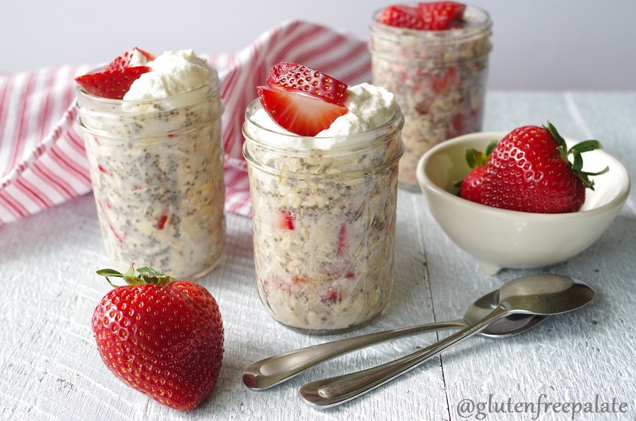 a close up of overnight oats with strawberries in a clear jar, topped with sliced strawberries