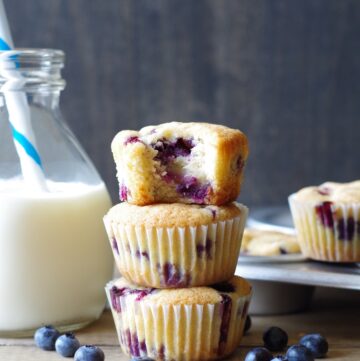 close up of three gluten-free blueberry muffins stacked, the muffin on the top has a bite out of it to show the texture