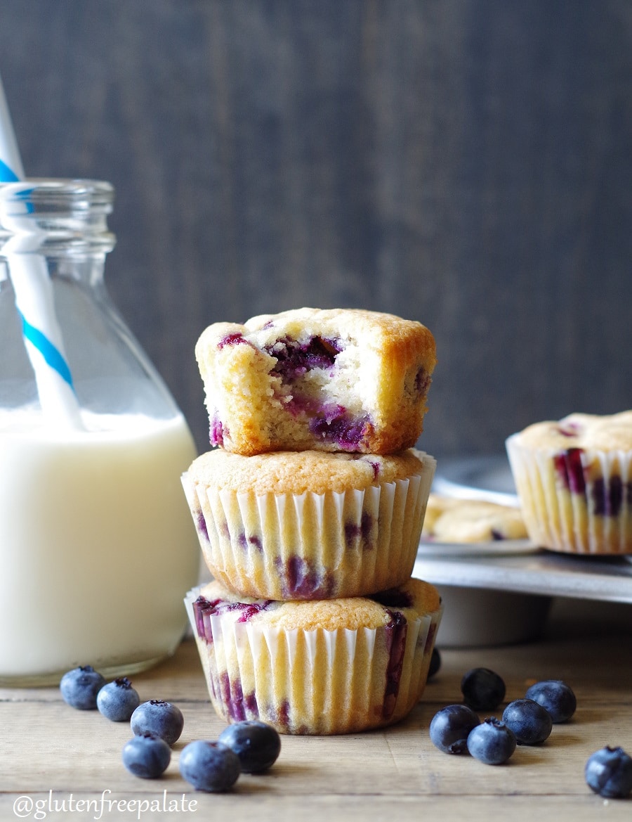 close up of three gluten-free blueberry muffins stacked, the muffin on the top has a bite out of it to show the texture