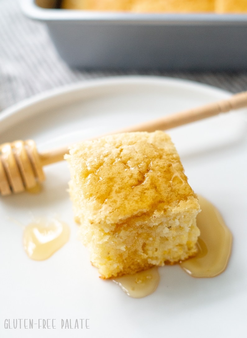 A slice of gluten-free cornbread on a white place with a honey drizzle.