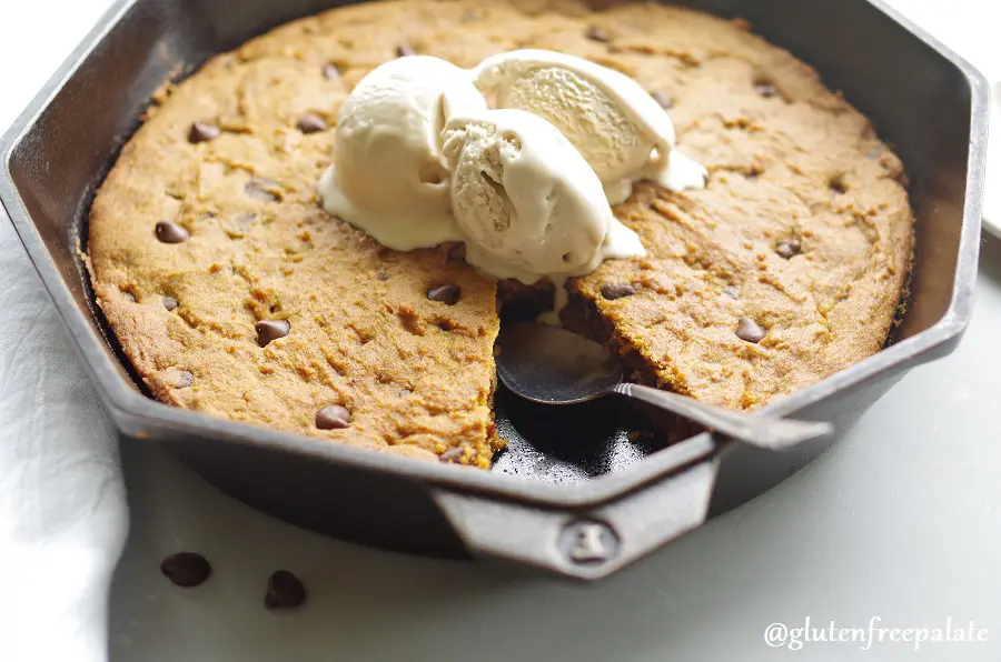 a side view of gluten free pumpkin chocolate chip skillet cookie in a cast iron skillet topped with three scoops of vanilla ice cream