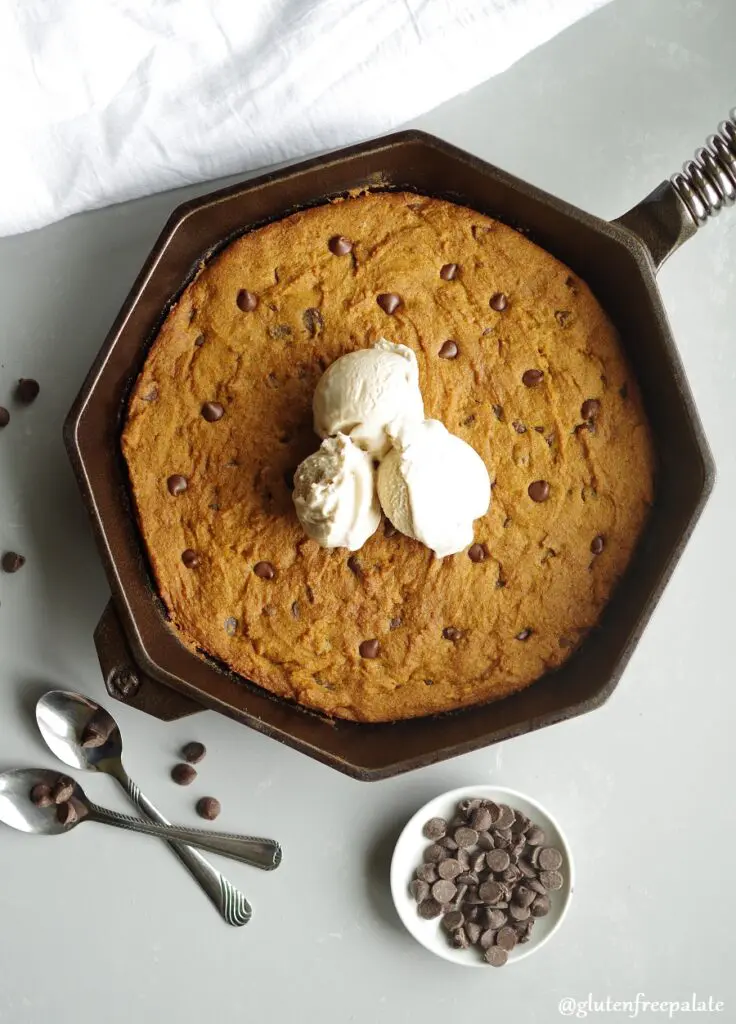 gluten free pumpkin chocolate chip skillet cookie in a cast iron skillet topped with three scoops of vanilla ice cream