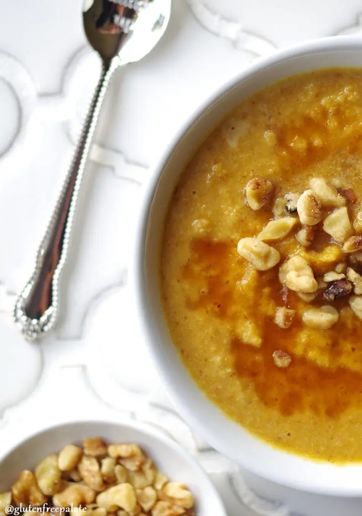 a close up of the side of a bowl of pumpkin porridge topped with chopped nuts, next to a spoon