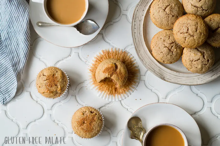 paleo snickerdoodle muffins on a white counter next to a cup of coffee and a plate of muffins