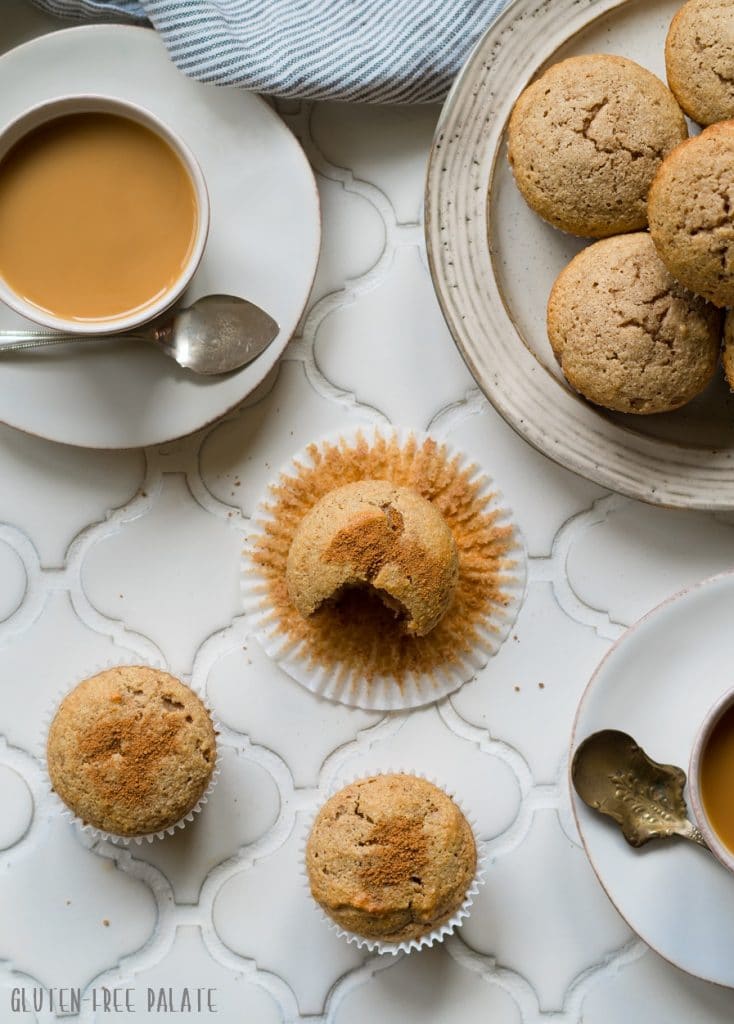 a top down view of paleo snickerdoodle muffins on a white counter next to a cup of coffee and a plate of muffins