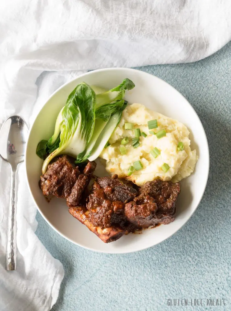 a top down view of instant pot short ribs, mashed potatoes and green vegerables next to a spoon.