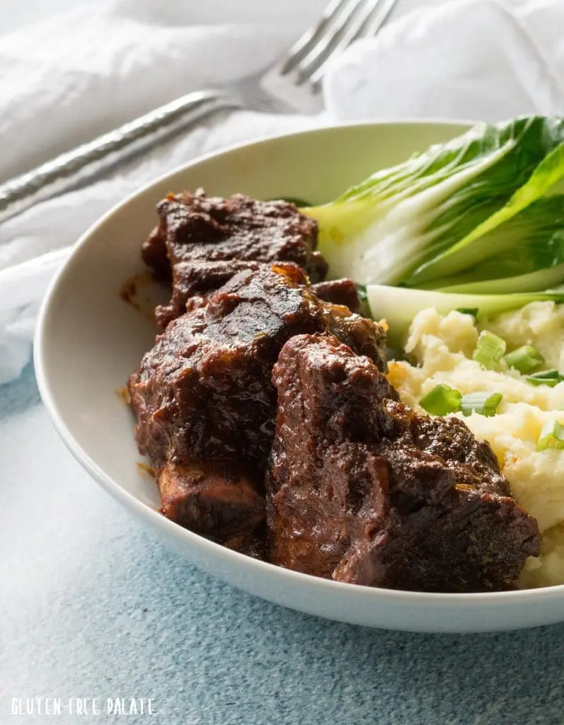 side view of beef short rib, mashed potatoes and green vegetables on a white plate
