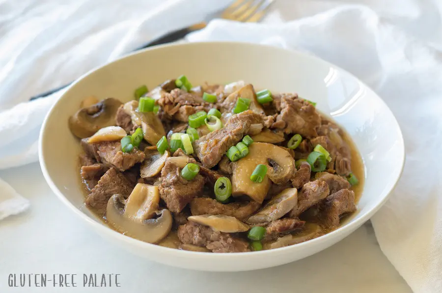 a side view of beef tips and mushrroms topped with sliced green onion on a white plate