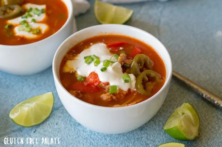 a close up of chicken soup topped with sour cream and green onion in a white bowl next to lime wedges - gluten-free instant pot recipes