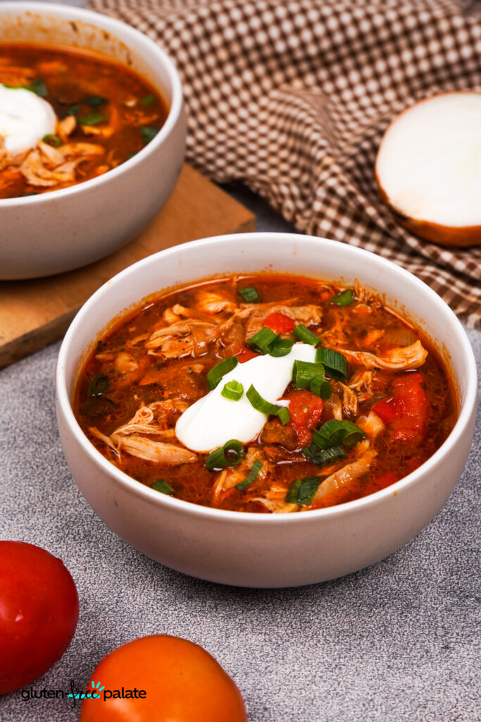A bowl of chicken fajita soup garnished with sour cream, chopped green onions.