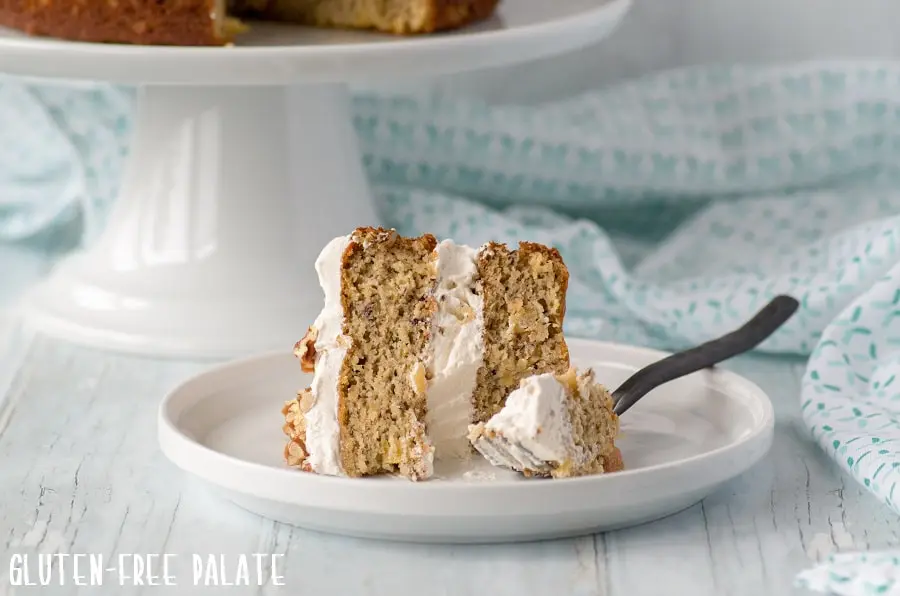 a close up of a slice of gluten-free hummingbird cake on a white plate with a fork