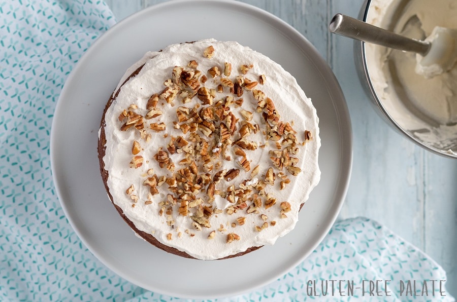 top down view of a grain-free hummingbird cake with white frosting and chopped pecans on top