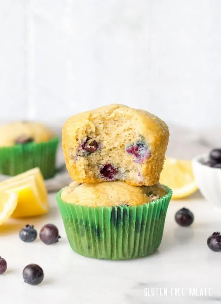 two paleo blueberry muffins stacked, the top muffin has a bite out showing the blueberries on the inside