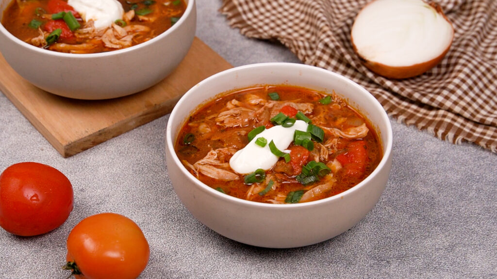 A bowl of chicken fajita soup garnished with sour cream, chopped green onions.