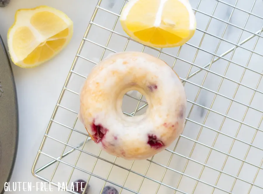 a lemon blueberry donut on a wire cooling rack next to lemon wedges