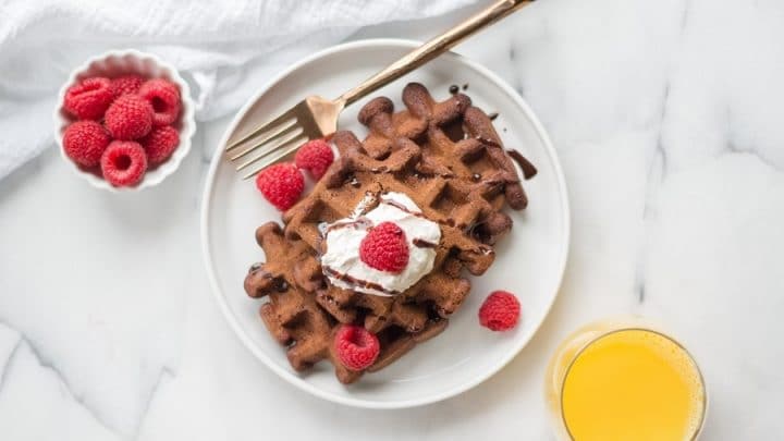 three gluten free chocolate waffles topped with whipped cream and raspberries
