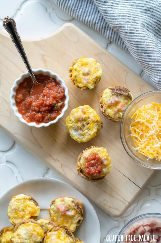 Mini Quiches on a cutting board next to a bowl of cheese and a bowl of salsa with a spoon