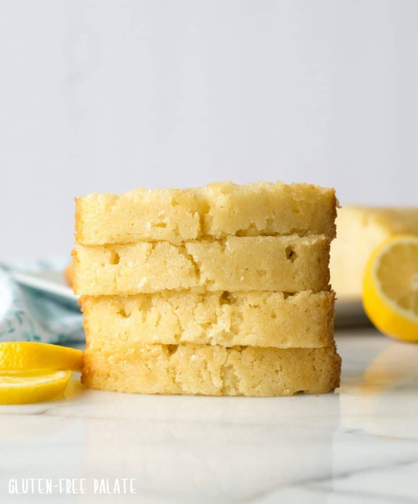 four slices of Gluten-Free Lemon Bread stacked on a marble slab next to lemon slices