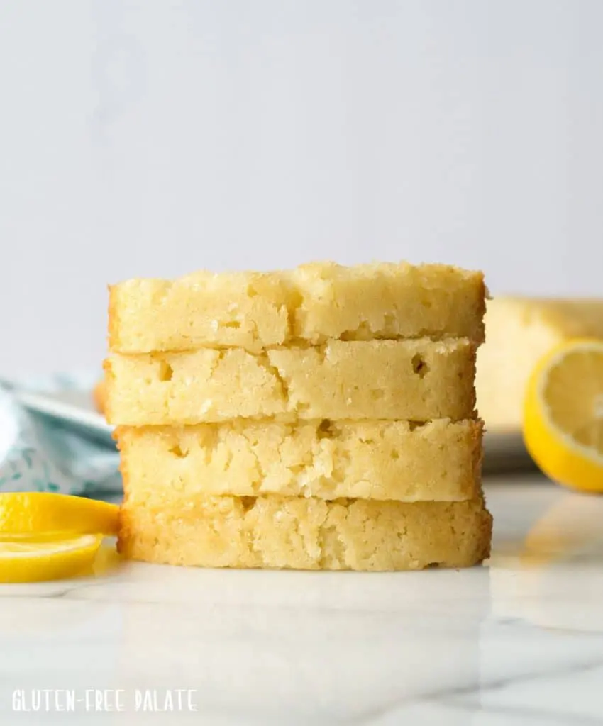four slices of Gluten-Free Lemon pound cake stacked on a marble slab next to lemon slices