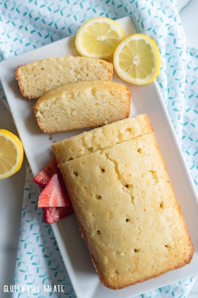 Gluten-Free Lemon Bread sliced on a white plate with slices of lemon on the side