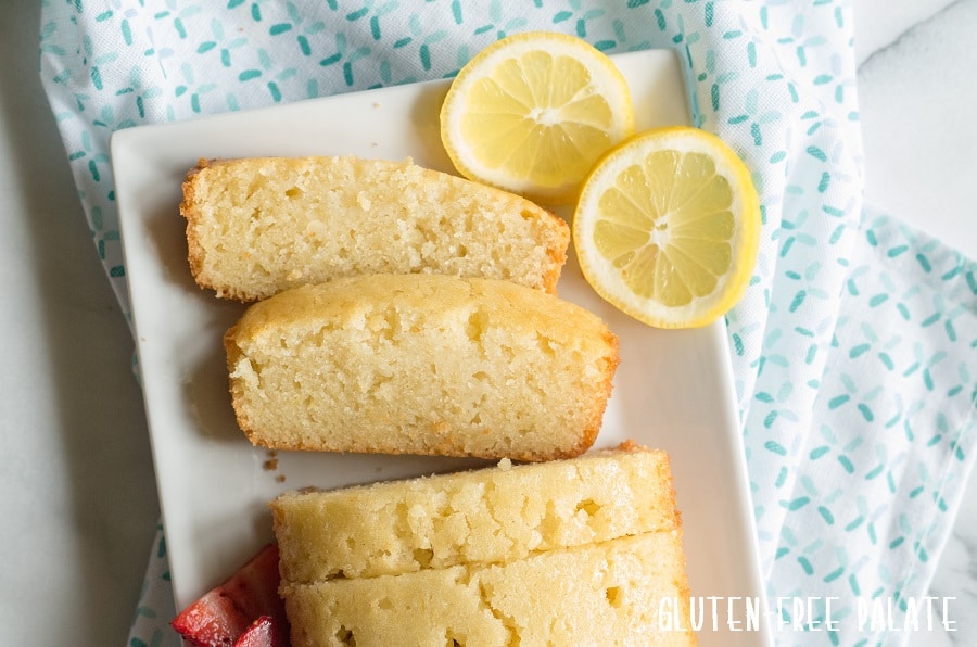a close up of Gluten-Free Lemon Bread sliced on a white plate with slices of lemon on the side