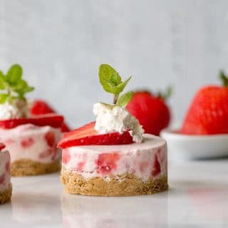 A close up of a mini strawberry cheesecake with whipped cream and a mint leaf on top.