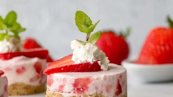 a close up of a mini strawberry cheesecake with whipped cream and a mint leaf on top