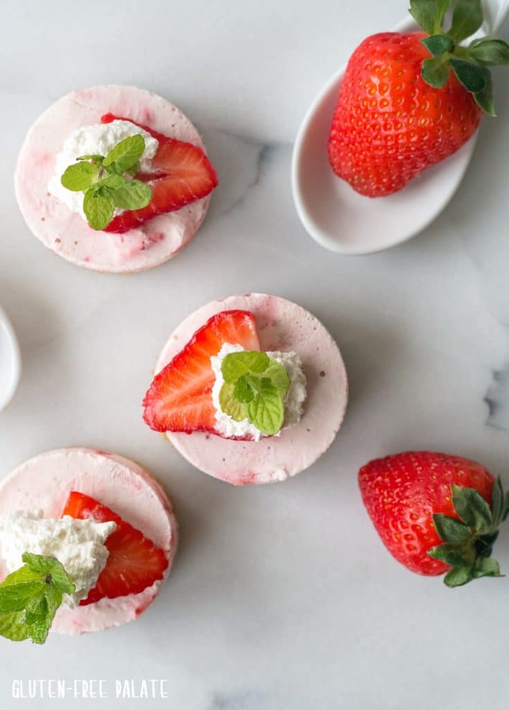 top down view of mini strawberry cheesecakes with whipped cream and a mint leaf on top
