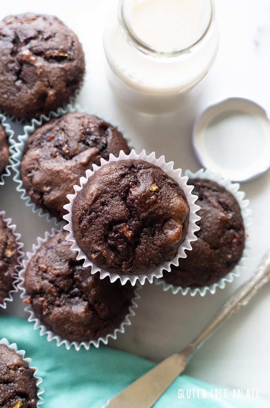 top down view of Grain-Free Chocolate Zucchini Muffins on a white background with a blue kitchen towl and a jar of milk