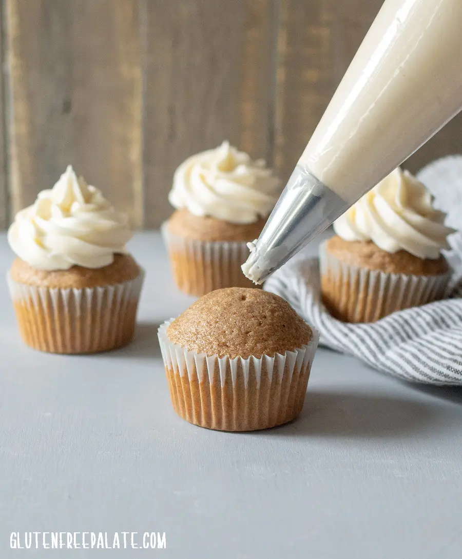 a chai cupcake with a piping bag, three chia cupcakes with frosting in the background