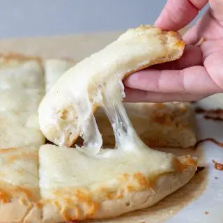 a close up of a hand holding a gluten-free bread stick with a cheese pull