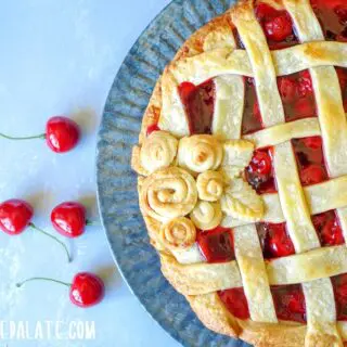 a close up of side view of Gluten-free Cherry Pie on a tin plate with scattered cherreis around it