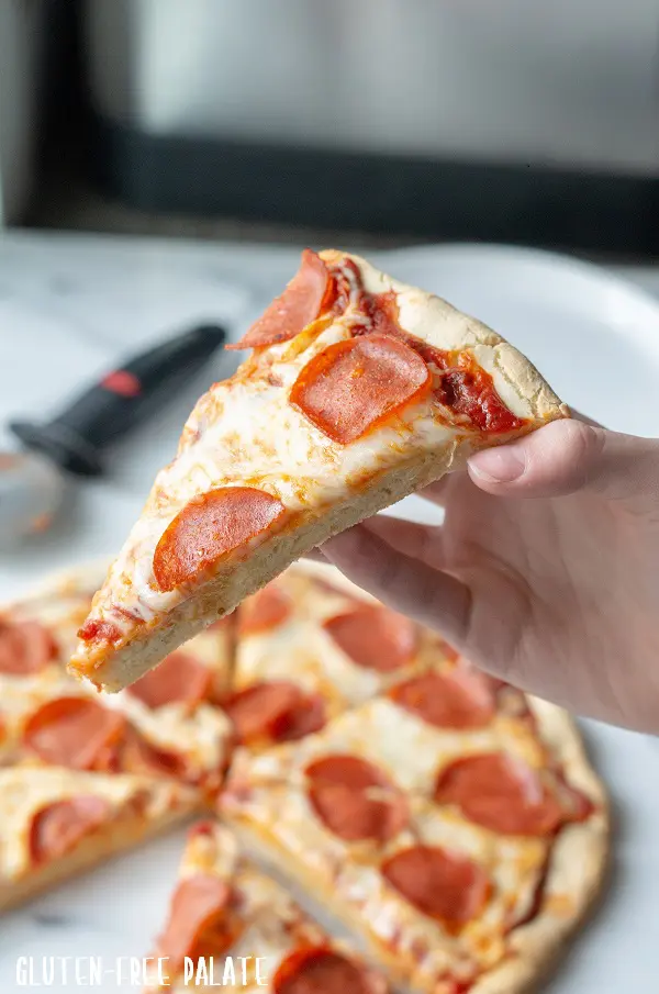 a hand holding a slice of gluten-free pepperoni pizza