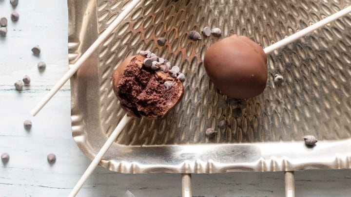 a close up of Gluten-Free Cake Pops covered in chocolate on a stick, on a metal tray