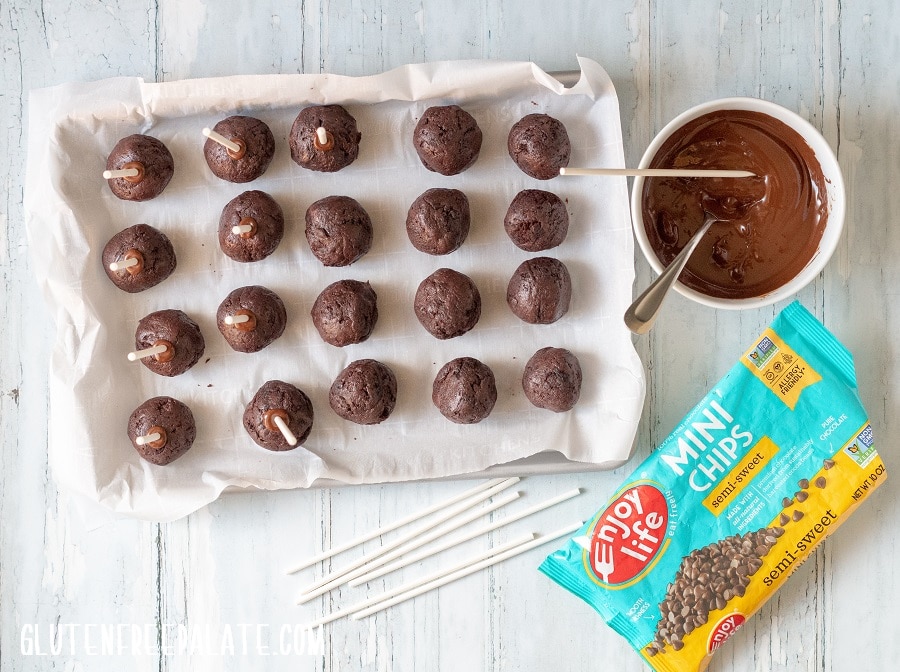 cake balls next to a bowl of melted chocolate and a bag of chocolate chips