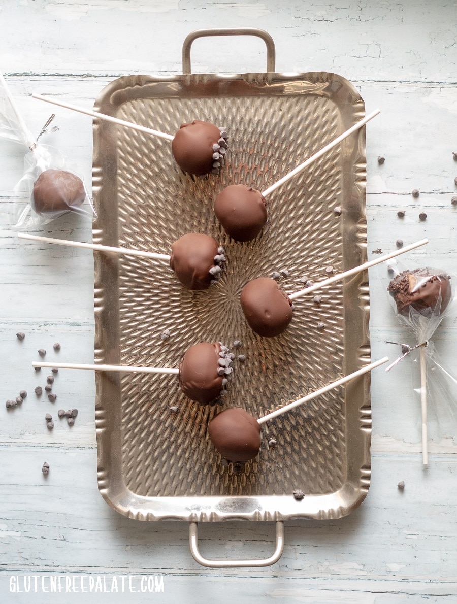 Gluten-Free Cake Pops covered in chocolate on a stick, on a metal tray, two are wrapped in plastic