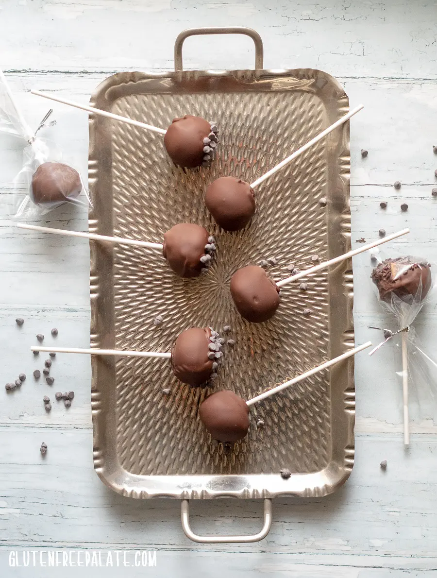 Gluten-Free Cake Pops covered in chocolate on a stick, on a metal tray, two are wrapped in plastic