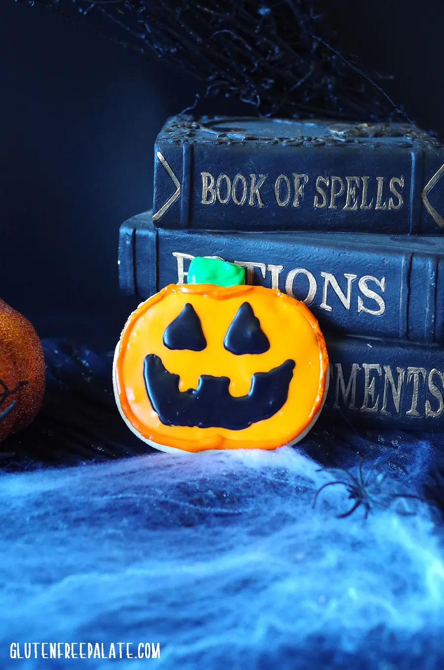 pumpkin cookie in front of books and a spider web for halloween
