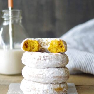 a close up of four gluten free pumpkin donuts stacked one with a bit out