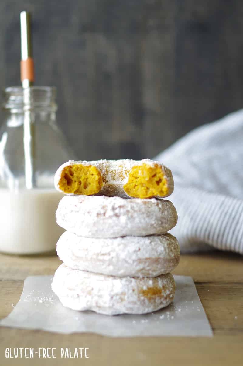 four gluten free pumpkin donuts stacked one with a bit out